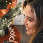 En la imagen, una mujer sonríe junto al árbol de Navidad.