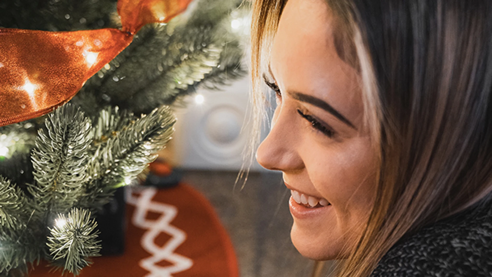 En la imagen, una mujer sonríe junto al árbol de Navidad.