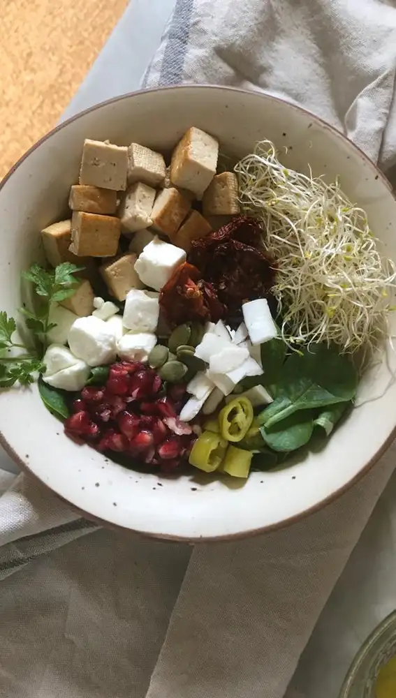 En la imagen, un bol saludable con espinaca, tofu marinado, guindilla, feta, brotes, granada y perejil.