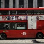 A traditional double decker red bus with an advert for "The Crown" drives through central London.