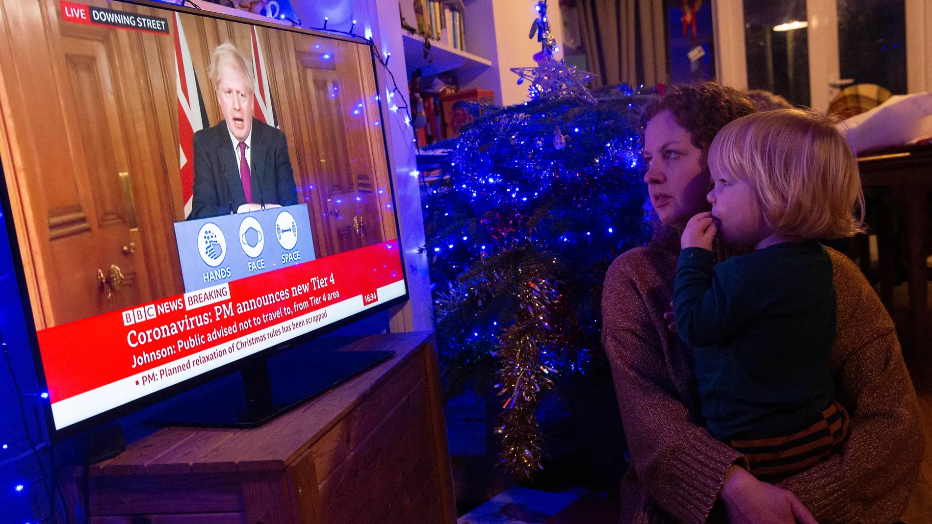 Dos británicos observan la comparecencia del primer ministro Boris Johnson esta tarde en la BBC anunciando más restricciones esta Navidad