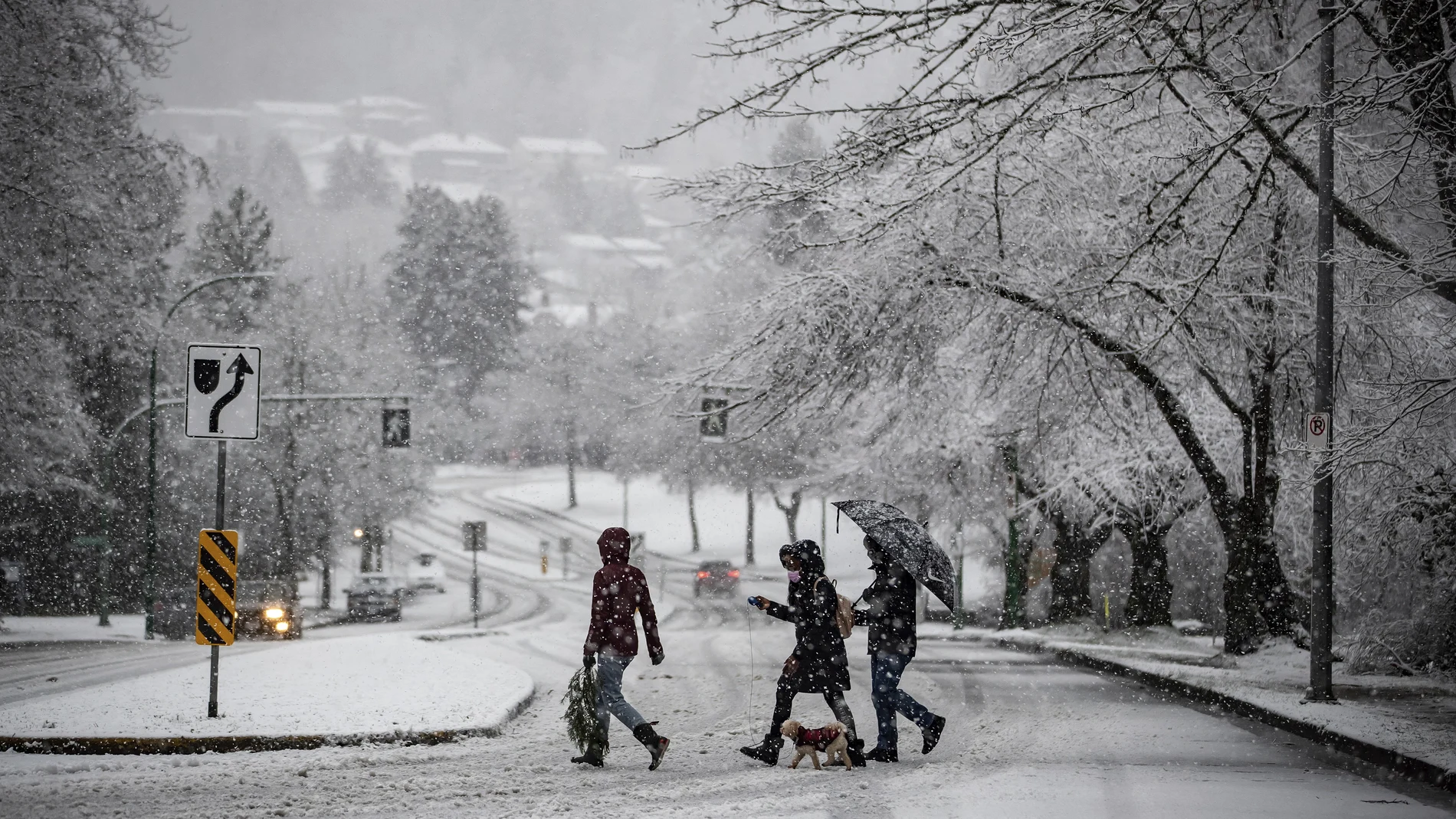 Heavy snow falls as people wearing face masks to curb the spread of COVID-19 crosses a road in Burnaby, British Columbia, on Monday, Dec. 21, 2020. Environment Canada issued a snowfall warning on the first day of winter. (Darryl Dyck/The Canadian Press via AP)
