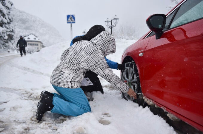 Una pareja pone las cadenas a las ruedas de su coche en una carretera del Pirineo aragonés
