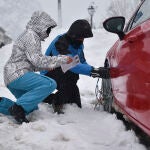 Dos personas ponen las cadenas a las ruedas de su coche en una carretera del Pirineo aragonés, en Huesca