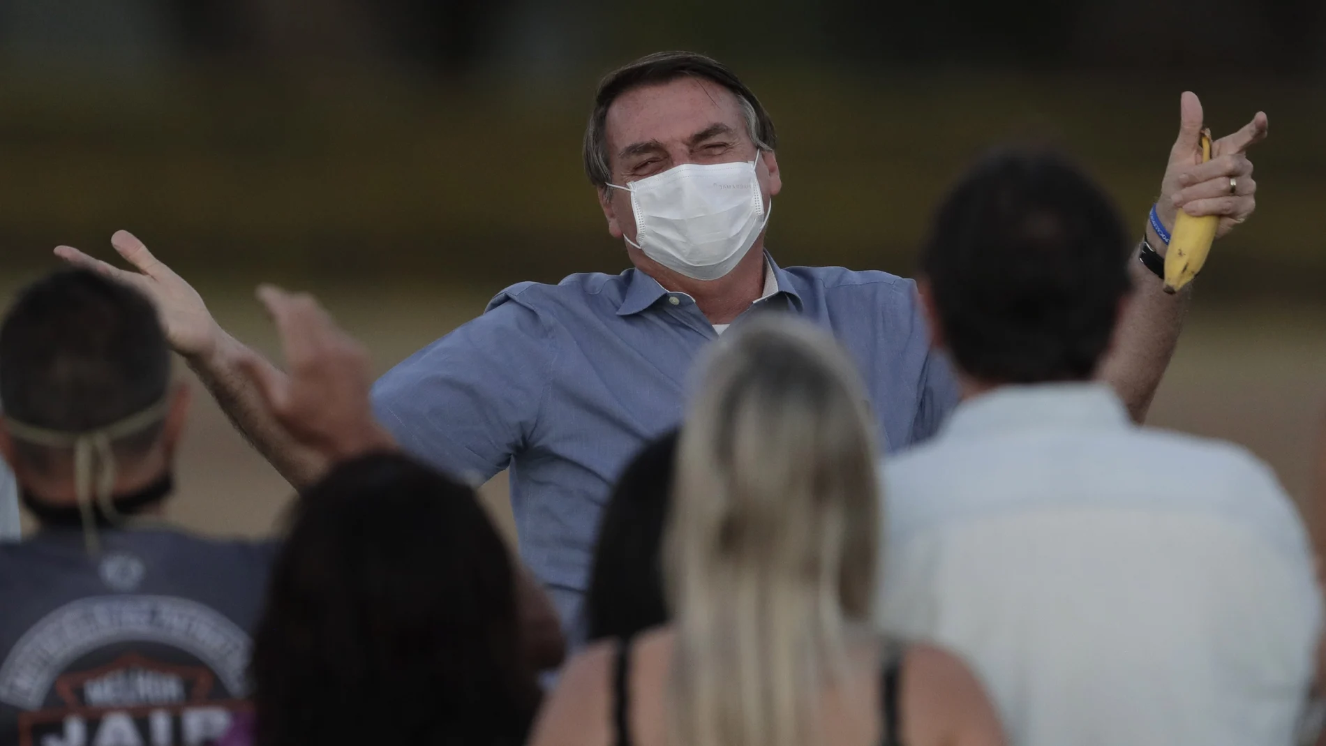FILE - in this July 24, 2020 file photo, Brazil's President Jair Bolsonaro, who is infected with COVID-19, wears a protective face mask as he talks with supporters during a Brazilian flag retreat ceremony outside his official residence the Alvorada Palace, in Brasilia, Brazil. The South American nation proud of its role as a regional leader in science, technology and medicine, finds itself falling behind its neighbors in the global race for immunization against a pandemic that has already killed nearly 200,000 of its people. (AP Photo/Eraldo Peres, File)