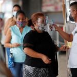 AME7712. CIUDAD DE PANAMÁ (PANAMÁ), 04/01/2021.- Un hombre mide la temperatura a una compradora en la entrada de un supermercado en la gran estación de San Miguelito hoy, en Ciudad de Panamá (Panamá). "La venta está regular. La gente está desabastecida tras días de encierro y sale a comprar, pero hay que ver cómo estará el movimiento en la semana", comentó a Efe Lester Herrera, un vendedor de legumbres en Ciudad de Panamá, donde desde este lunes rige una nueva cuarentena que busca frenar un vertiginoso repunte de la covid-19. EFE/ Bienvenido Velasco