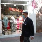 Un hombre protegido con mascarilla pasa junto a una tienda de ropa en la que se anuncian rebajas