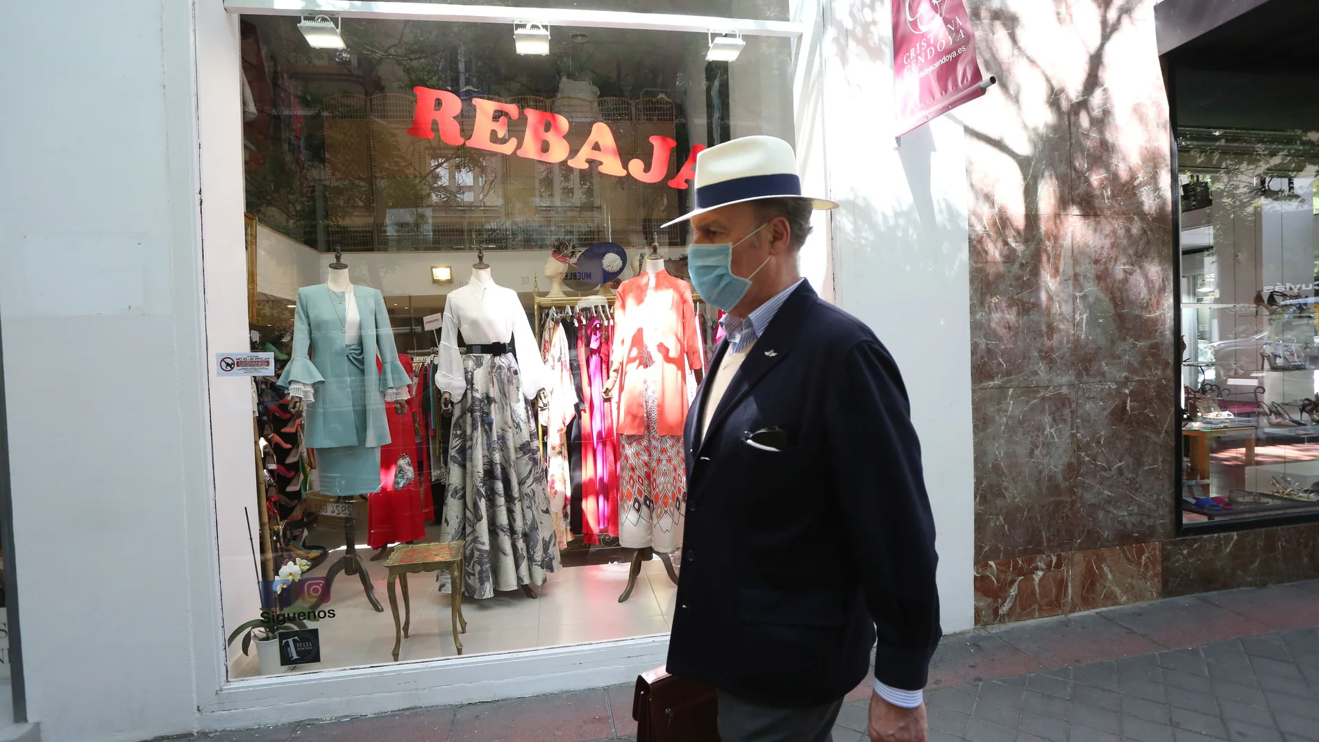 Un hombre protegido con mascarilla pasa junto a una tienda de ropa en la que se anuncian rebajas