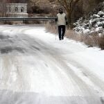 Un hombre pasea por un tramo de la carretera de acceso al embalse de Fuentes Claras con placas de hielo