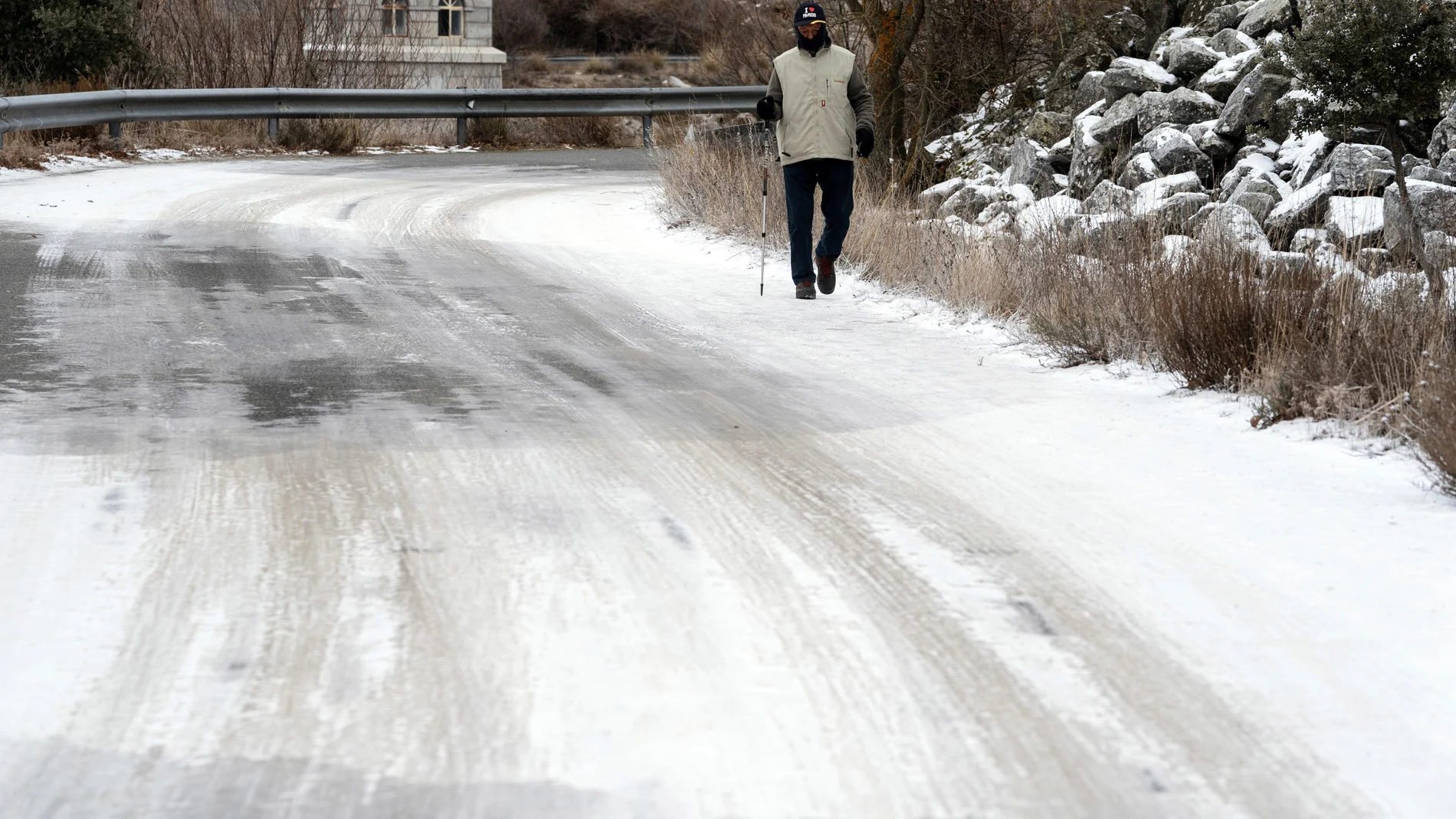 Un hombre pasea por un tramo de la carretera de acceso al embalse de Fuentes Claras con placas de hielo