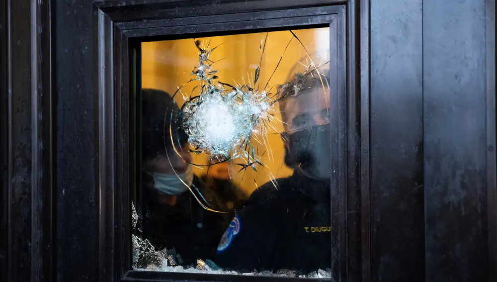 Dos policías observan a través del vidrio roto de una de las puertas del Capitolio de Estados Unidos, luego de que seguidores de Donald Trump irrumpieran en el recinto durante unas protestas en Washington (Estados Unidos).