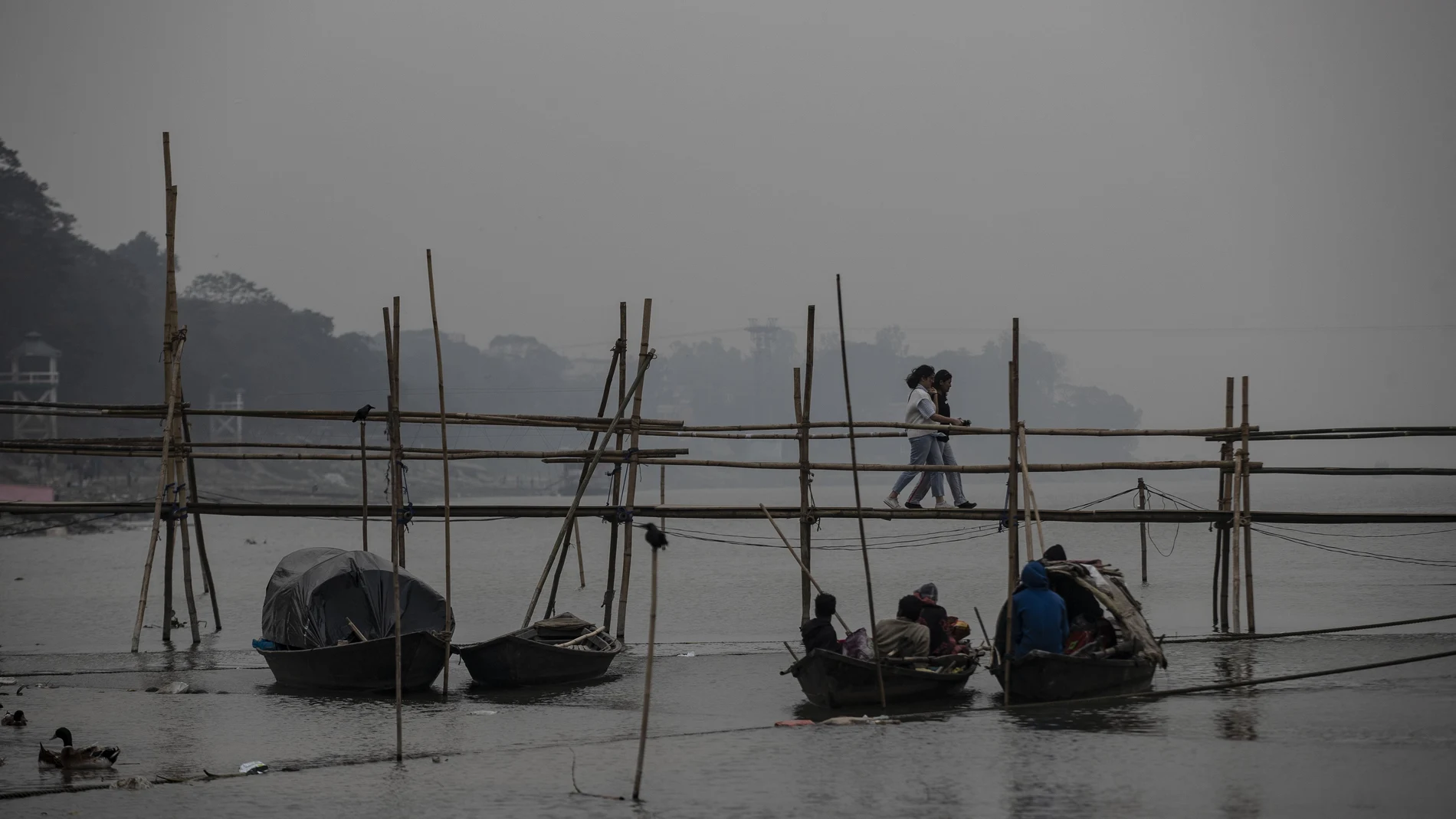 Indian girls walk on a temporary footbridge to board on a ferry as fishermen take rest in their boats in the river Brahmaputra in Gauhati, in the northeastern state of Assam, India, Monday, Jan. 11, 2021. Brahmaputra is one of Asia's largest rivers, which passes through China's Tibet region, India and Bangladesh before converging into the Bay of Bengal. (AP Photo/Anupam Nath)