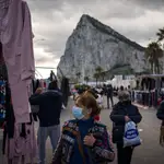 Gente con mascarilla pasea por un mercadillo con el peñón de Gibraltar al fondo.