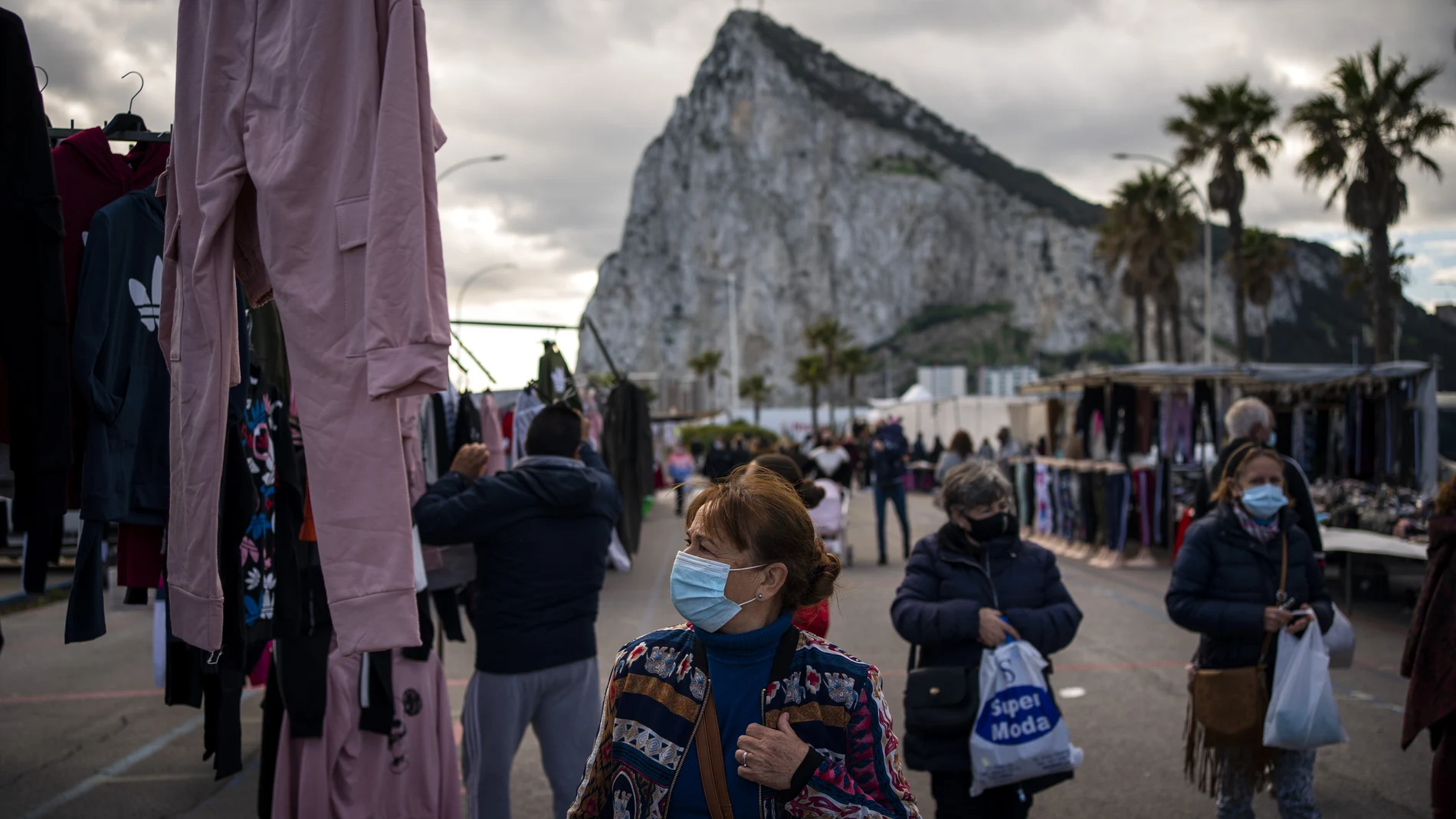 Gente con mascarilla pasea por un mercadillo con el peñón de Gibraltar al fondo.