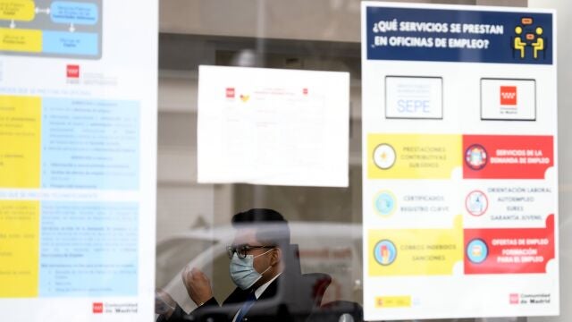 Un hombre con mascarilla tras el cristal de la puerta de una oficina de empleo, SEPE