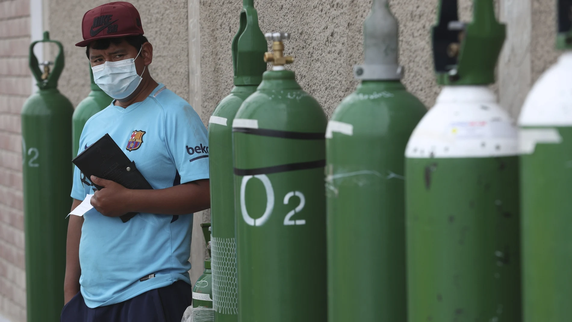 A man waits by his empty oxygen tank in a line of other customers outside a shop that refills them in the Villa El Salvador shantytown of Lima, Peru, Thursday, Jan. 21, 2021, amid the COVID-19 pandemic. (AP Photo/Martin Mejia)