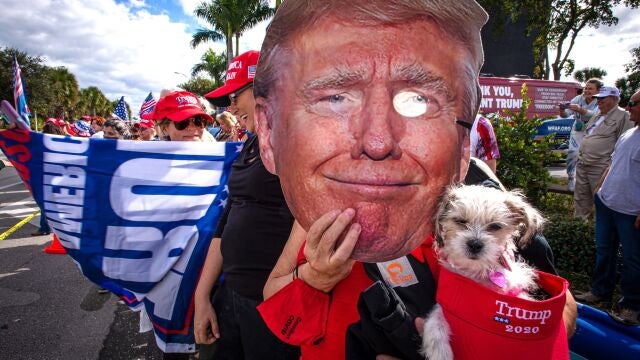 Una persona sostiene una máscara con la imagen del presidente Donald Trump mientras espera su llegada este miércoles en West Palm Beach