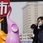 Residents wearing masks to curb the spread of the coronavirus stand near the Chinese character for "Market" in Wuhan, China, Tuesday, Jan. 26, 2021. The central Chinese city of Wuhan, where the coronavirus was first detected has largely returned to normal but is on heightened alert against a resurgence as China battles outbreaks elsewhere in the country. (AP Photo/Ng Han Guan)