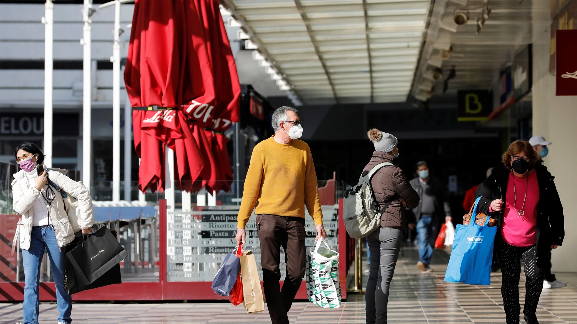 Varias personas cargadas con bolsas de la compra pasean por el exterior de un centro comercial