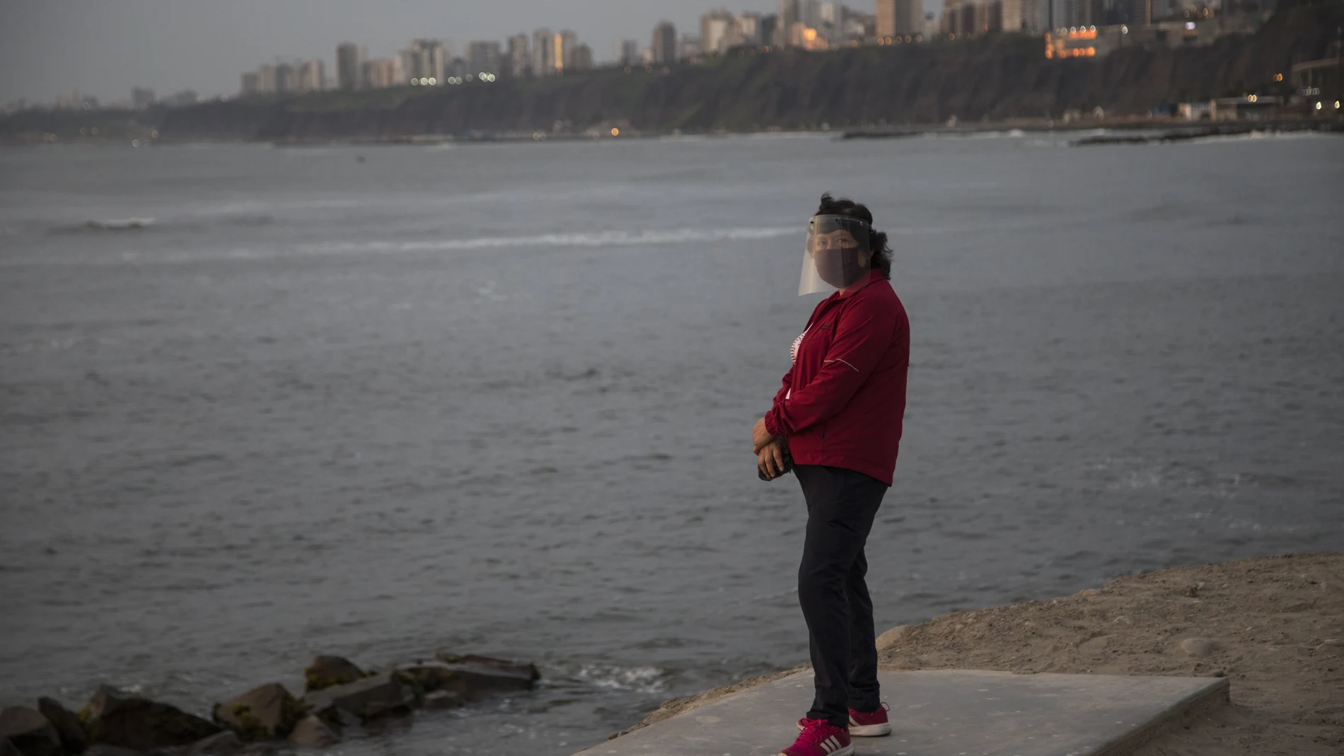 A woman wearing a mask and face shield to curb the spread of the new coronavirus stands on a platform overlooking the Pacific Ocean in Chorrillos, Lima, Peru, Tuesday, Jan. 26, 2021. (AP Photo/Rodrigo Abd)