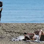 Un agente de policía indica a una mujer la obligatoriedad de la mascarilla también en la playa, como esta del Postiguet en Alicante
