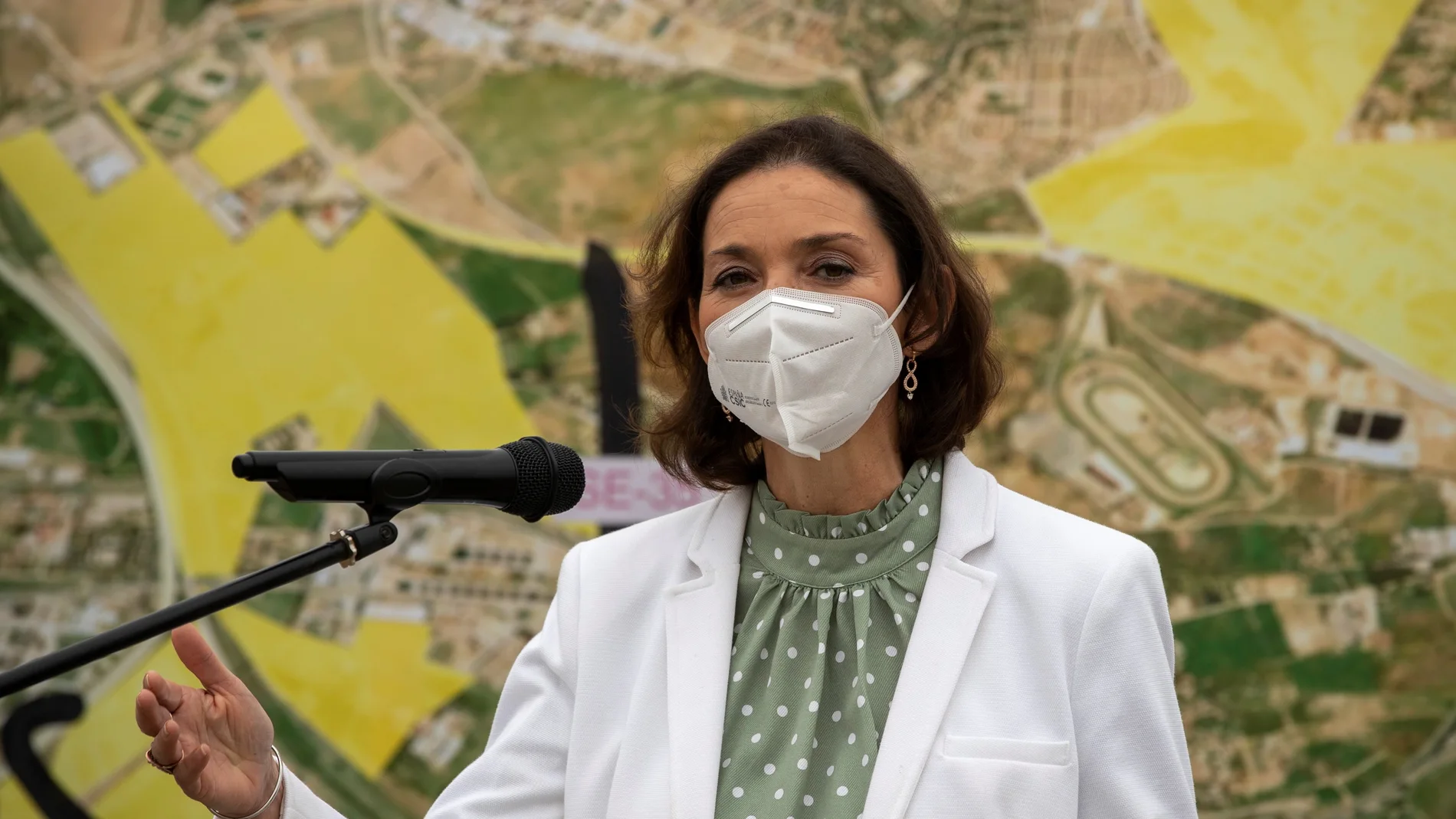 La ministra de Industria, Comercio y Turismo, Reyes Maroto, atiende a los medios ante un panel informativo durante su visita a los terrenos donde se ubicará el Parque Empresarial Megapark en Dos Hermanas (Sevilla)