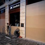Dos operarios tapan las cristaleras de una oficina del Caixabank en la plaza del Ayuntamiento de Valencia como medida de protección frente a las protestas por la detención del rapero Pablo Hasél