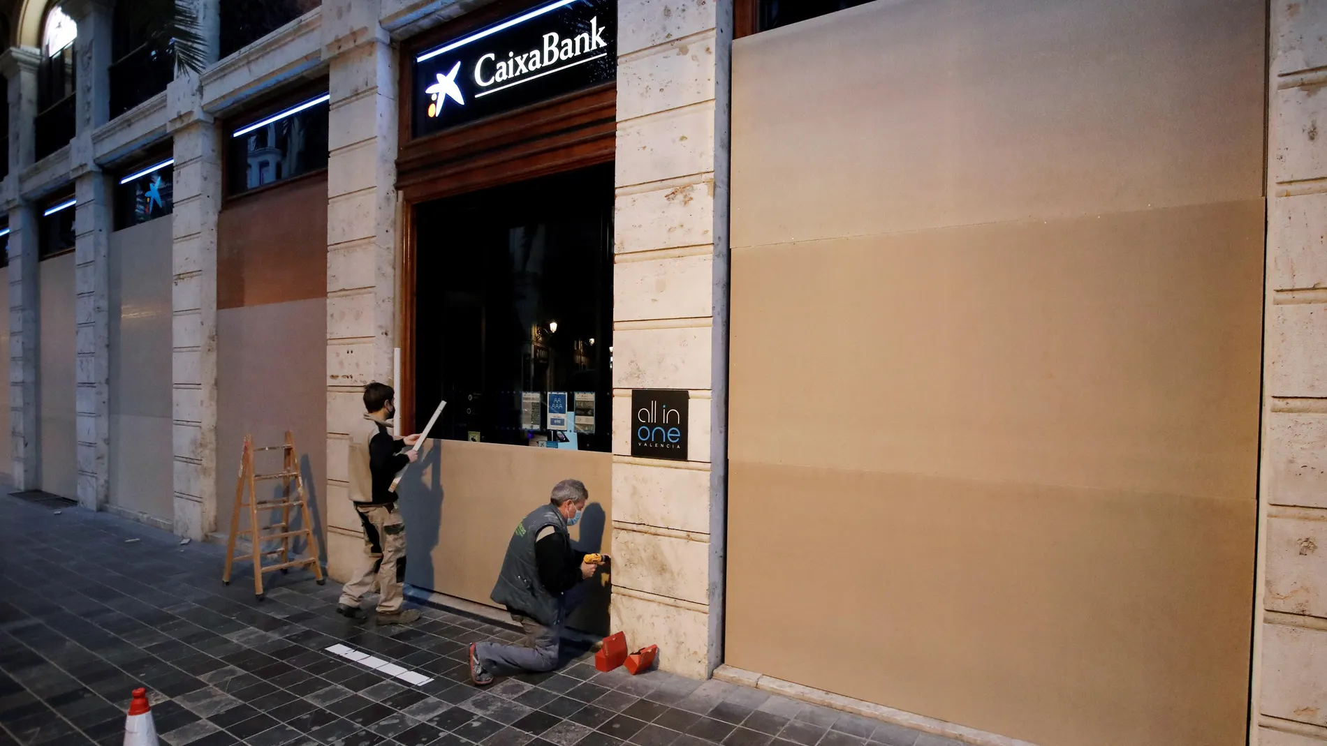 Dos operarios tapan las cristaleras de una oficina del Caixabank en la plaza del Ayuntamiento de Valencia como medida de protección frente a las protestas por la detención del rapero Pablo Hasél