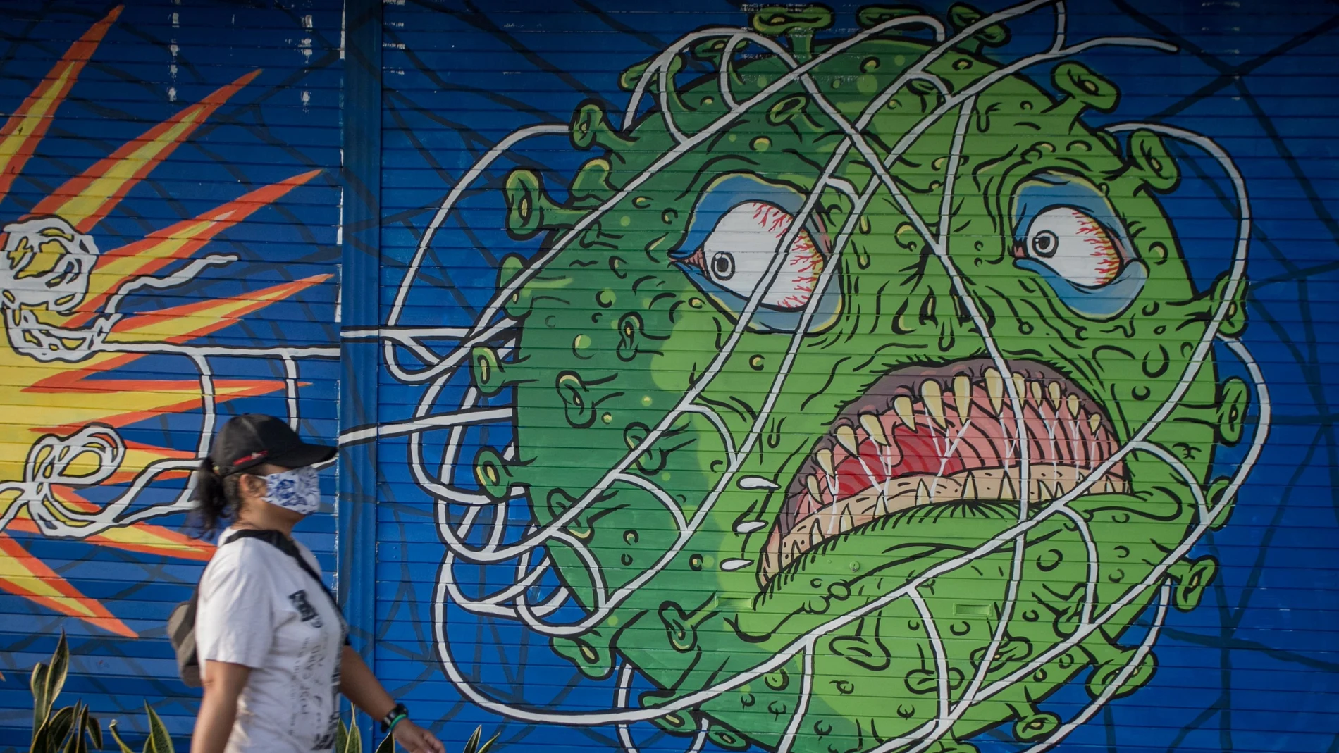 Una mujer pasa bajo un dibujo callejero del virus de la covid 