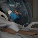 Una sanitaria agarra la mano de un paciente de coronavirus mientras habla por teléfono con sus familiares en un hospital de Los Ángeles