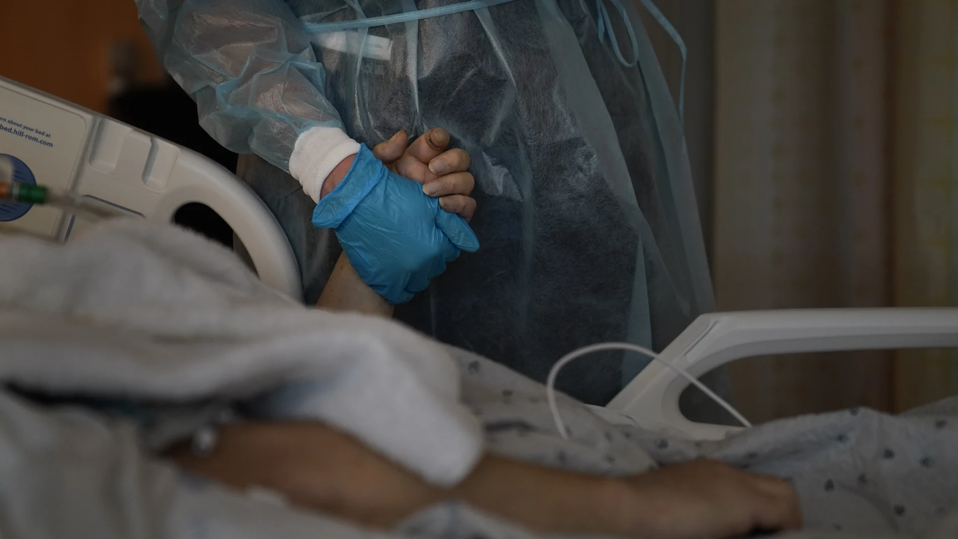 Una sanitaria agarra la mano de un paciente de coronavirus mientras habla por teléfono con sus familiares en un hospital de Los Ángeles