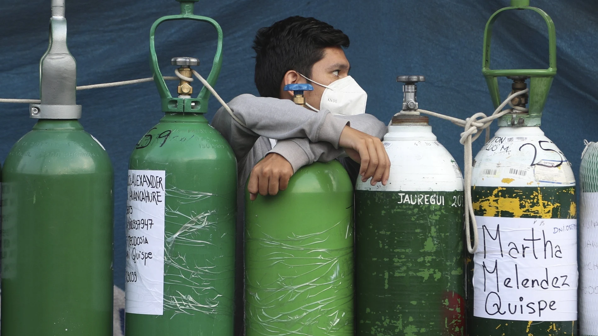 A man leans on his empty oxygen cylinder waiting for a refill shop to open in the San Juan de Lurigancho neighborhood of Lima, Peru, Monday, Feb. 22, 2021, as the lack of medical oxygen to treat COVID-19 patients continues to be the norm nationwide. Long lines form outside private providers with many spending the night outside so as to not lose their place in line. (AP Photo/Martin Mejia)