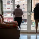 Dos personas mayores miran por la ventana de su vivienda