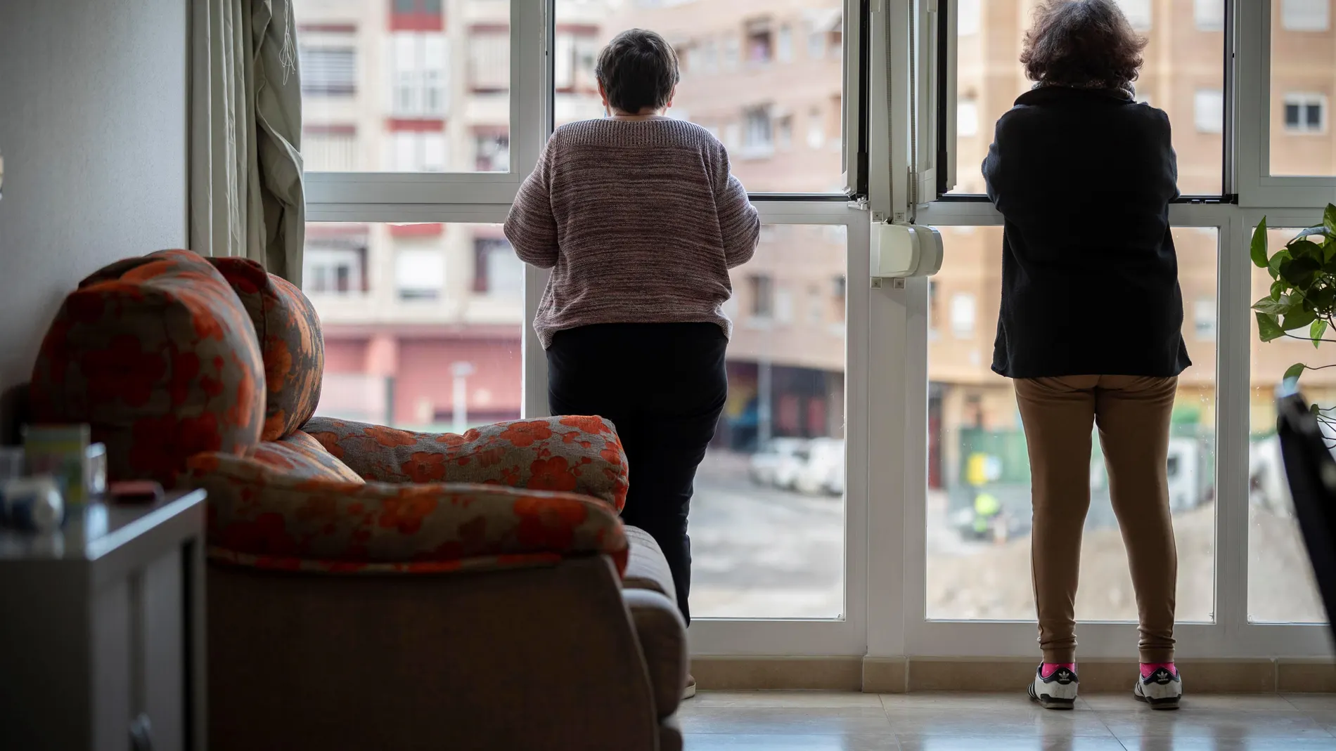 Dos personas mayores miran por la ventana de su vivienda