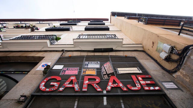 Imagen de la entrada de un garaje privado en Madrid, en el que cuelga la para en rojo "Garaje", y en el que se encuentran numerosos carteles de se vende y se alquila plaza de garaje para coche o moto.