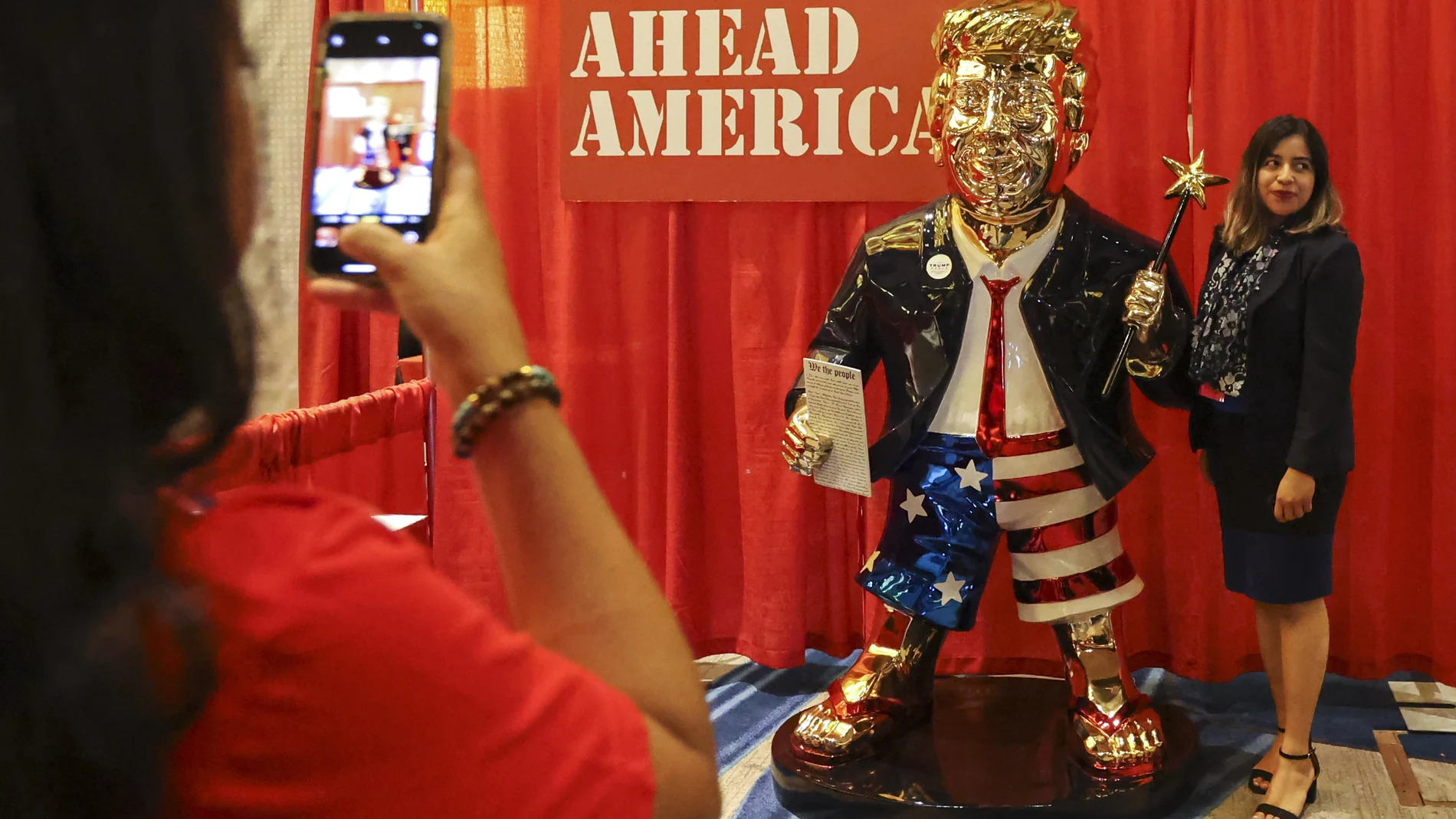 Una mujer se hace una foto con el Donald Trump dorado en el congreso conservador en Orlando, Florida