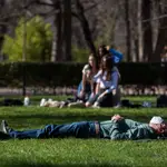 Imagen de un hombre echándose la siesta sobre el césped del parque a pleno sol y con la mascarilla puesta
