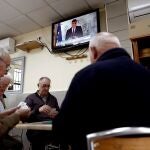Un grupo de ancianos juega a las cartas en un bar del barrio de Aluche, en Madrid, mientras en la televisión comparece el presidente del Gobierno tras un Consejo de Ministros extraordinario en el que se ha abordado la crisis del coronavirus.