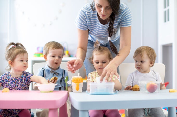 Grupo de bebés de la guardería que comen alimentos saludables a la hora del almuerzo junto con el jardín de infancia