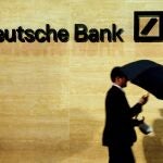 Un hombre abre un paraguas ante una sucursal de Deutsche Bank