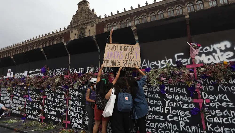 Mujeres colocan flores y carteles con nombres de víctimas por feminicidios, en el muro metálico instalado por el Gobierno en Ciudad de México