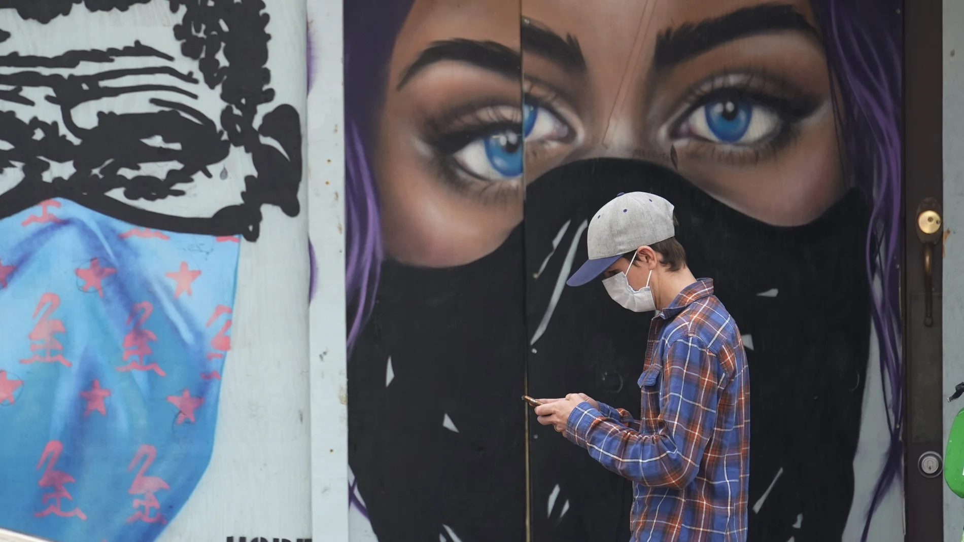 Un joven con mascarilla pasea frente a un grafiti en Austin, Texas