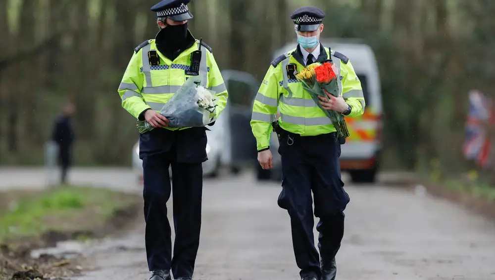 Dos agentes de Policía llevan flores a la entrada del club de golf en la que se está investigando la desaparición de Sarah Everard en Ashford
