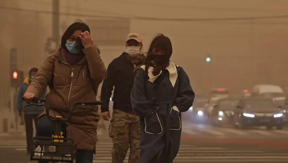 Personas con mascarillas caminan por una calle de la capital golpeada por aire contaminado y tormenta de arena