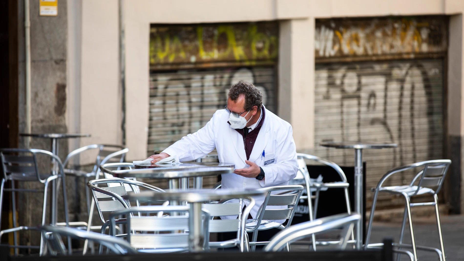 Un camarero limpia las mesas de una terraza con la mascarilla puesta en el centro de Madrid