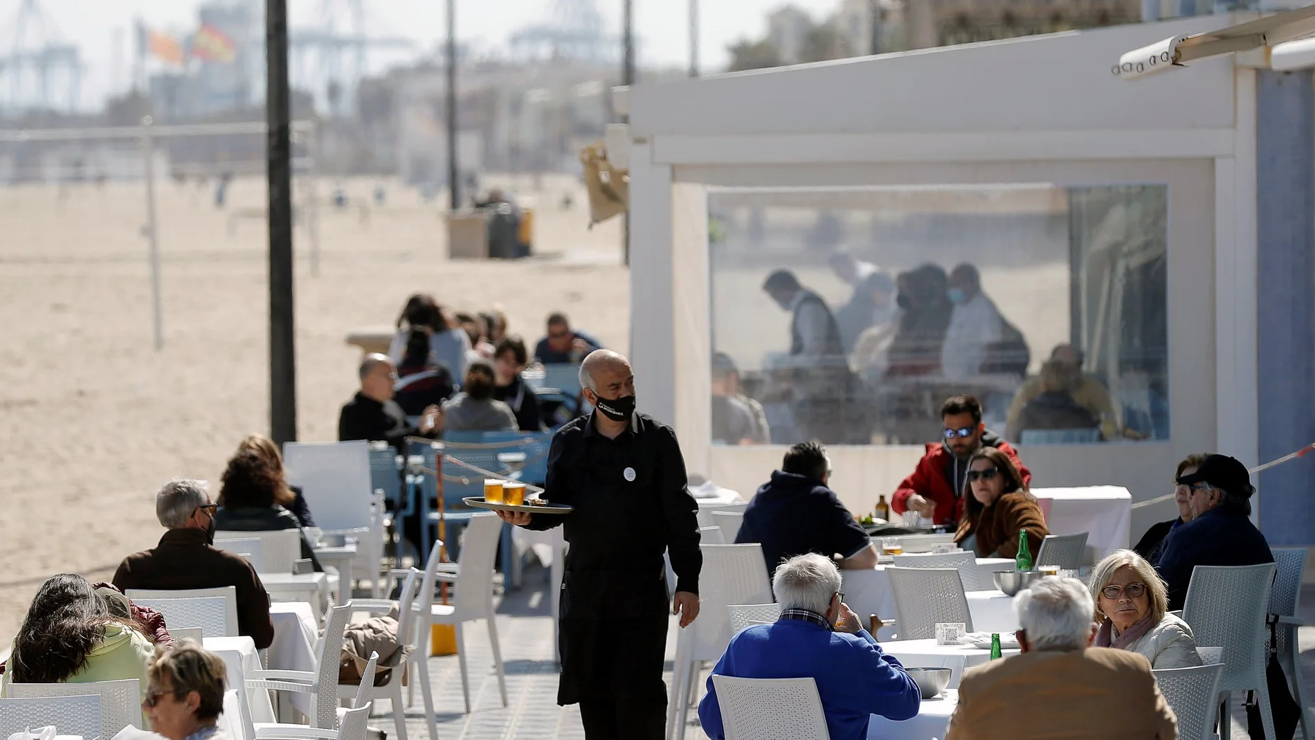 Un camarero atiende las mesas de una terraza en uno de los restaurantes de la playa de la playa de la Malvarrosa de Valéncia