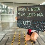 AME3085. BRASILIA (BRASIL), 16/03/2021.- Una mujer muestra un cartel de protesta en el que se lee "Brasil no tiene cama en la UCI" en referencia al colapso hospitalario debido al recrudecimiento de la pandemia, frente a la entrada del Ministerio de Salud hoy, en Brasilia (Brasil). Brasil es considerado actualmente el epicentro global de la crisis sanitaria y ya suma más de 11,5 millones de contagios, con cerca de 280.000 muertes y una situación agravada por una variante amazónica, que es al menos tres veces más contagiosa que la original y ya se ha expandido por todo el país. EFE/ Joédson Alves
