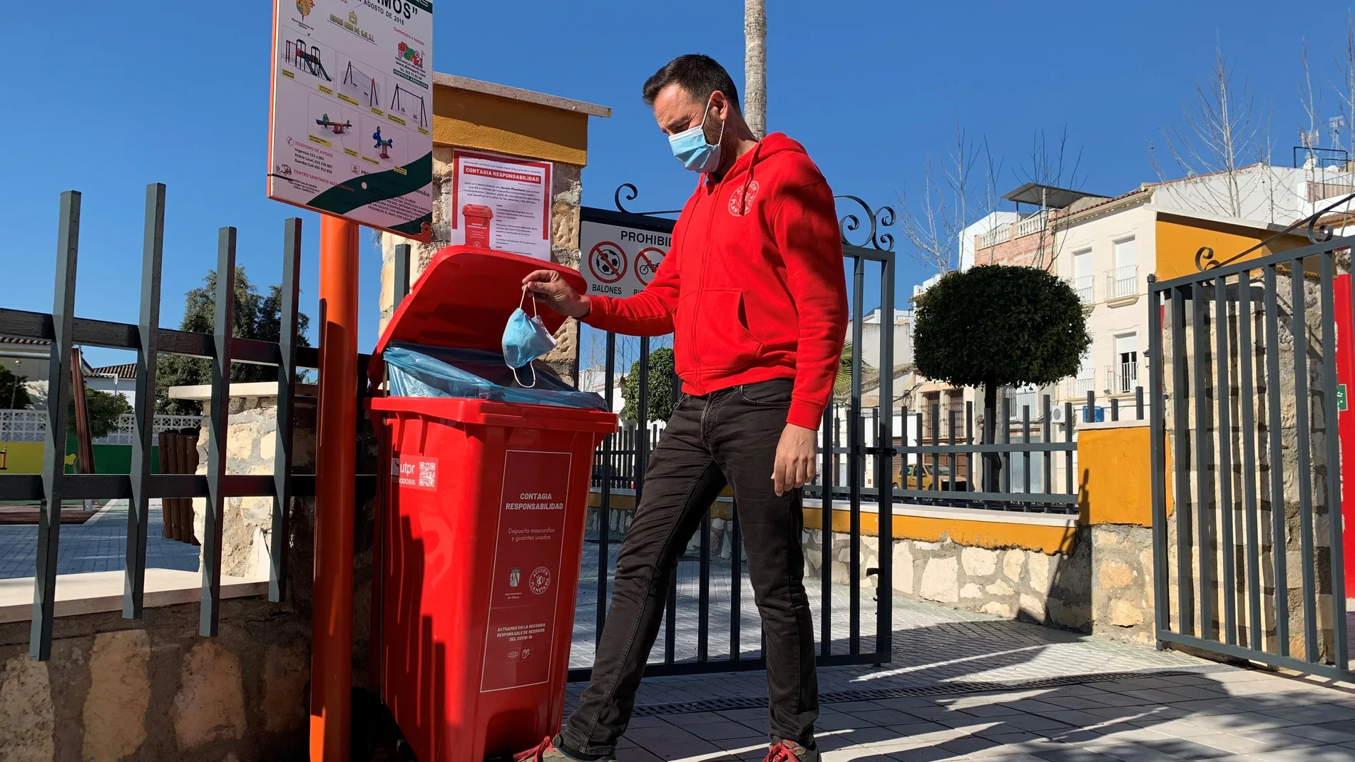 Un hombre echa una mascarilla dentro de un contenedor de color rojo que tiene como único fin recoger las mascarillas y guantes en Gilena (Sevilla).EFE/Fermín Cabanillas