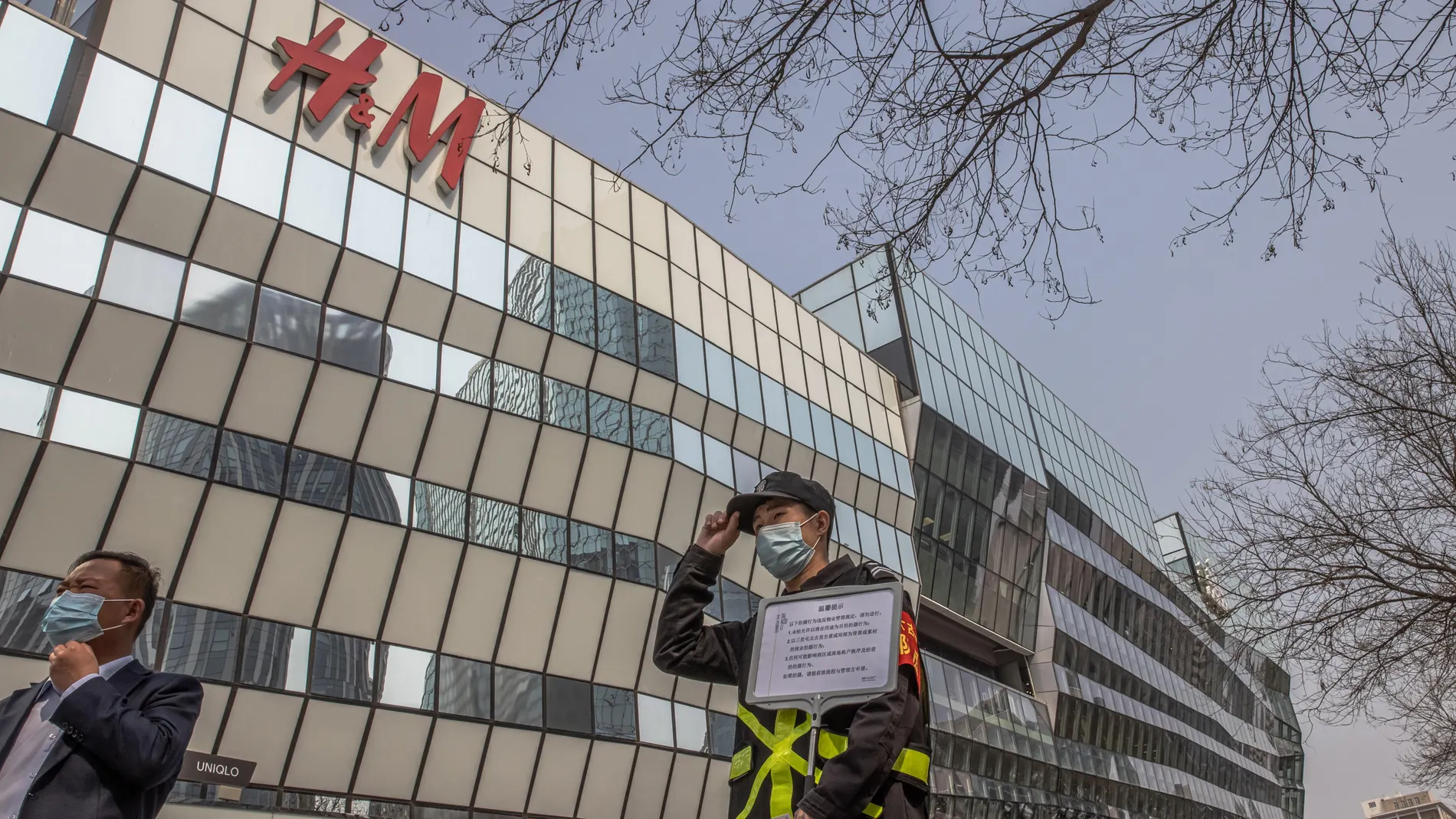 Un oficial de seguridad sostiene un cartel que dice "No se permiten fotos para uso comercial" frente a una tienda H&M en una zona comercial de Sanlitun en Pekín
