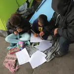 Un solicitante de asilo ayuda a sus hijos a hacer sus deberes en un campo en Los Cerros (Tijuana)